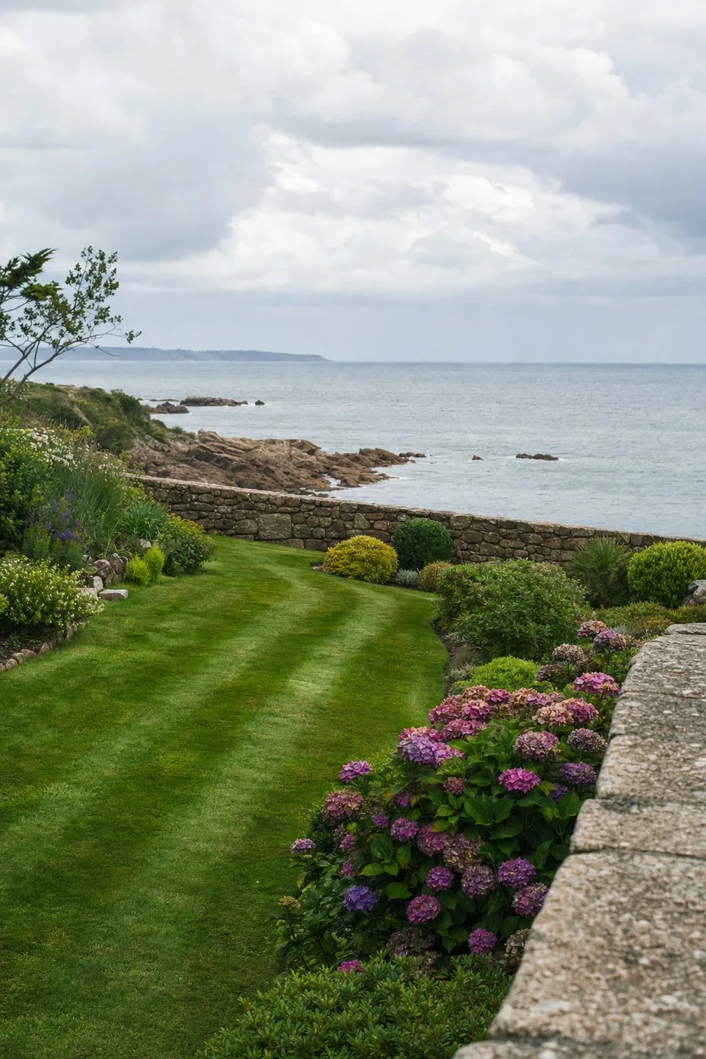 Jardin de bord de mer entretenu, pelouse tondue, hortensias et muret de granit.